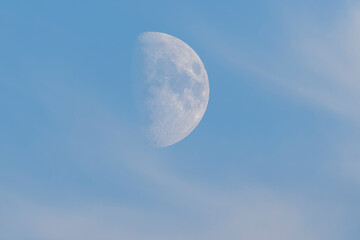 The rising moon on a soft blue sky with light clouds.