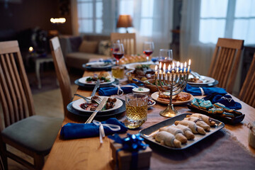 Lit menorah on dining table prepared for family meal on Hanukkah.