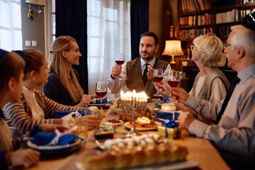 Jewish father toasting to his extended family at dining table during Hanukkah celebration.