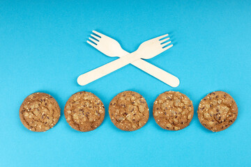 five pieces of oatmeal cookies are laid out in a row, crossed wooden forks on top of the cookies