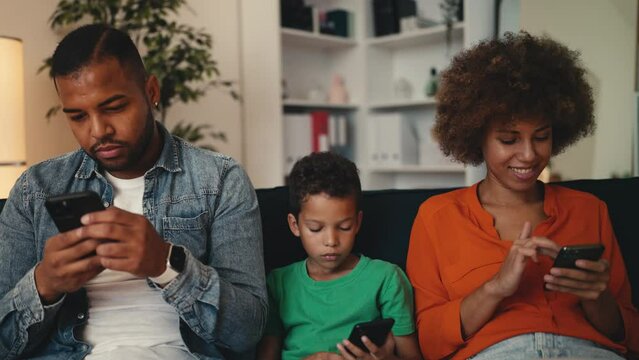 Gadget-addicted family using their smartphones on couch ignoring communication. Mother, father and little son scrolling their smartphones at home