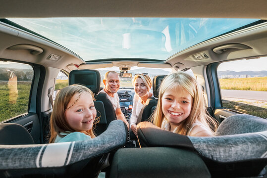 Young couple with daughters portrait sitting in a modern car with a transparent roof. Happy family moments, childhood, fast food eating or auto journey lunch break concept image.