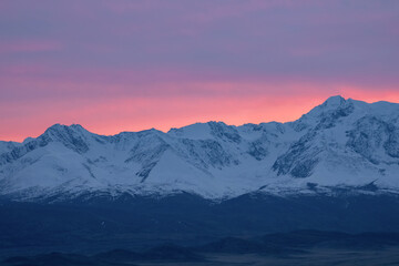 Soft pink light glides over the snow-capped peaks of the mountains in the early morning. Beautiful...