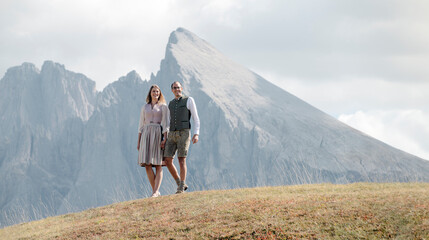 Mann und Frau stehen Hand in Hand in Tracht inmitten der Berge der Dolomiten