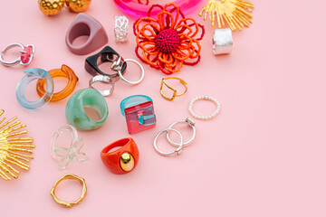 Colorful trendy bijouterie on pink background. Fashion silver, golden and plastic, acrylic and ceramic rings, bracelets and earrings. Stylish accessories. Women's jewelry. - obrazy, fototapety, plakaty