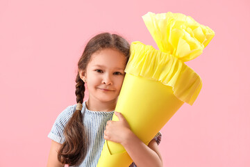 Happy little girl with yellow school cone on pink background