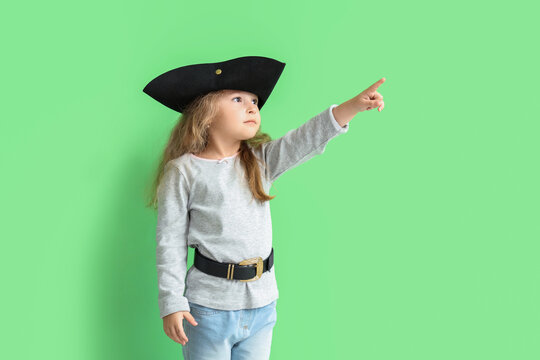 Cute little girl dressed as pirate pointing at something on green background