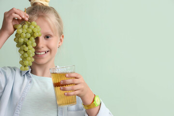 Little girl with glass of juice and grapes on green background