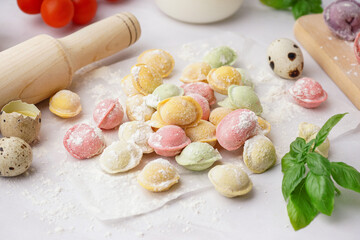 Baking paper with colorful raw dumplings and basil on white background