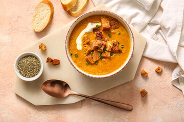 Bowl of tasty cream soup with croutons and bread on beige background