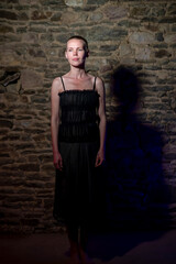 Capturing the essence of a middle-aged woman, approximately 40, donning a black dress and a stylish short hairstyle, illuminated by intense light against a brick wall background
