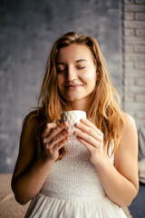 With a delightful smile, the young lady enjoys her coffee, appreciating the morning bliss. This image encapsulates the tranquil ambiance of morning coffee rituals