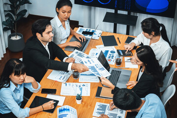 Wide top view of diverse group of business analyst team analyzing financial data report paper on meeting table. Chart and graph dashboard by business intelligence analysis. Meticulous
