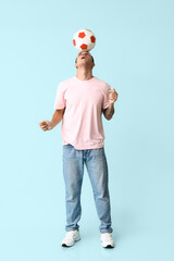 Handsome young man playing with soccer ball on blue background