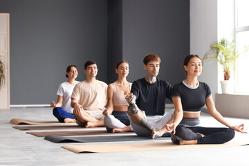 Fototapeta premium Group of sporty young people meditating in gym