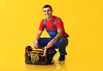 Male car mechanic taking wrench from tools bag on yellow background
