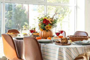 Pumpkin with autumn bouquet on festive dining table in room, closeup
