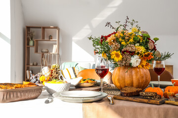 Pumpkin with autumn bouquet on festive dining table in room, closeup
