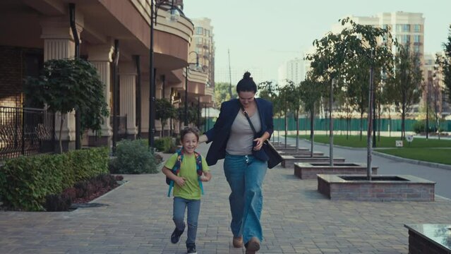 A schoolboy with a backpack runs to school with his mother along the city street. The child rushes to the classroom for the lesson. High quality 4k footage