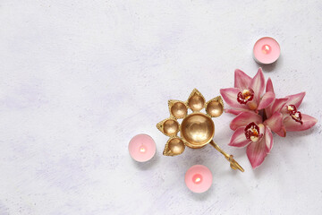 Diya lamp with burning candles and beautiful orchid flowers on grunge white background. Divaly celebration