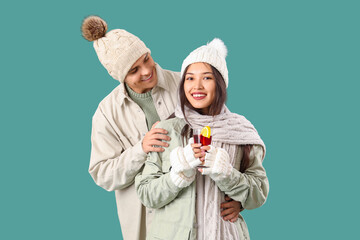 Happy couple in warm clothes with glass of tasty mulled wine on turquoise background