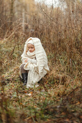 Portrait of a smiling young girl sitting in a park wrapped in a white blanket.