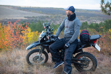 Fototapeta na wymiar caucasian man in gloves and cap sitting near a motorbike in the forest at sunset light