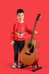 Cute little Asian boy with guitar on red background