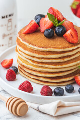 Stack of fresh pancakes with strawberries and blueberries drizzled with maple syrup and honey. Healthy traditional American breakfast on the white background