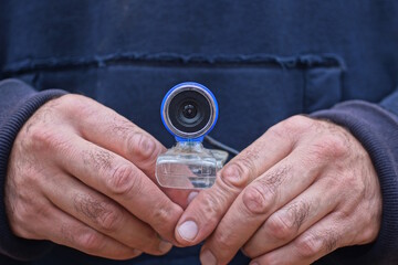 a man in blue clothes holds a small webcam on the street
