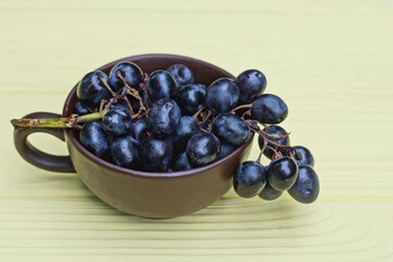 fresh blue ripe grapes on a branch in a brown ceramic cup stands on a yellow wooden table