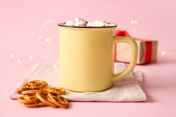 Cup of hot cocoa with marshmallows and pretzels on pink background