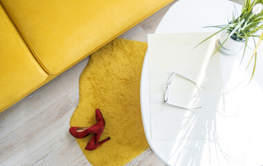 red women's high-heeled shoes lie on the floor in the room near the yellow sofa and table, top view