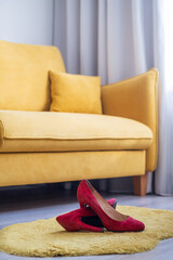 red women's high-heeled shoes lie on the floor in the room near the yellow sofa