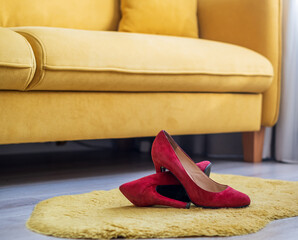 red women's high-heeled shoes lie on the floor in the room near the yellow sofa
