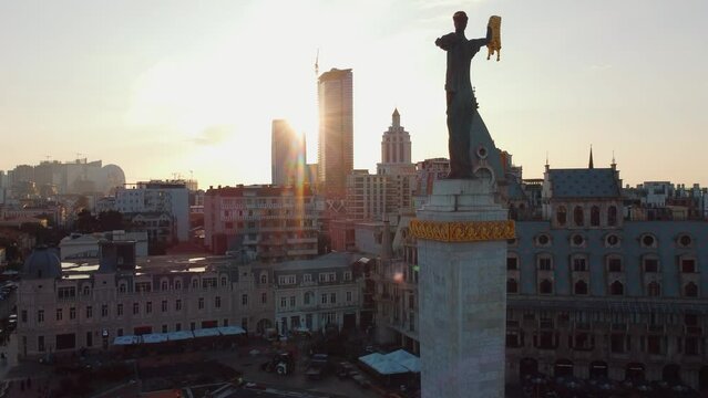 Batumi, Georgia - August 8, 2022.: Circular aerial view from drone in rays of sun at sunset around statue of Medea on Europe Square in popular tourist spot of Batumi in summer.