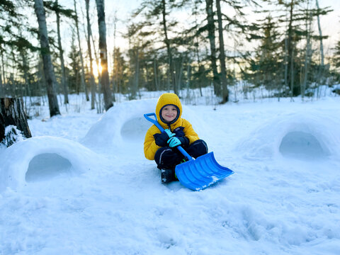 A boy with a shovel built igloos of snow in the backyard in sunset.