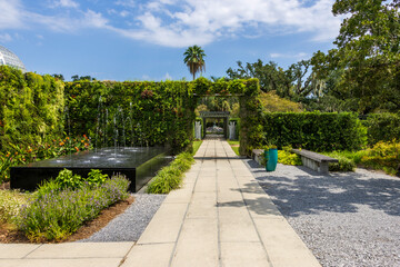 a footpath in the garden with a black marble water fountain and lush green trees and plants and...