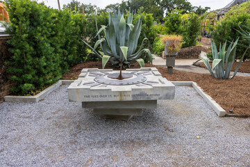 a gorgeous summer landscape at New Orleans Botanical Garden with a sundial surrounded by gravel and...