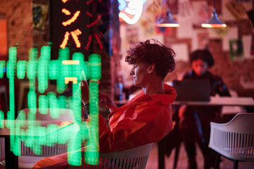 Side view of young man in bomber jacket scrolling on tablet screen while sitting in cyberpunk bar...