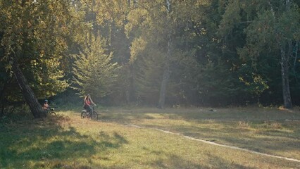 The family actively spends time in the park riding bicycles. Mother and son are riding together on paths in nature. High quality 4k footage