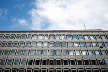 An old office building with many windows and a blue sky with white clouds in Oslo, Norway. Reflections in the windows