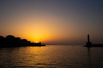 Fototapeta premium Sunset landscape in Chania's harbour with lighthouse silhouette on quiet Mediterranean waters