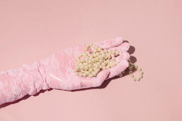 A hand in a lace glove, pearl beads in it, an elegant, romantic pastel pink composition.
