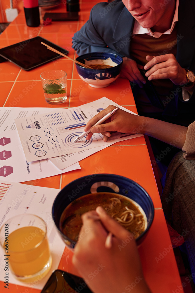 Poster hand of young businesswoman with pen pointing at financial document with graphic data while discussi