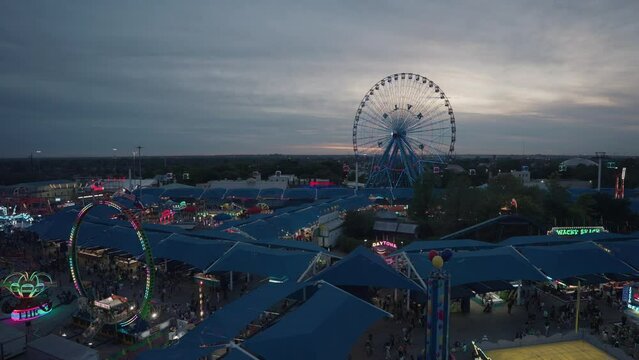 Aerial View of Dallas Cityscape and Fair Carnival Looking at The Rides, Ferris Wheel and Crowds in the evening