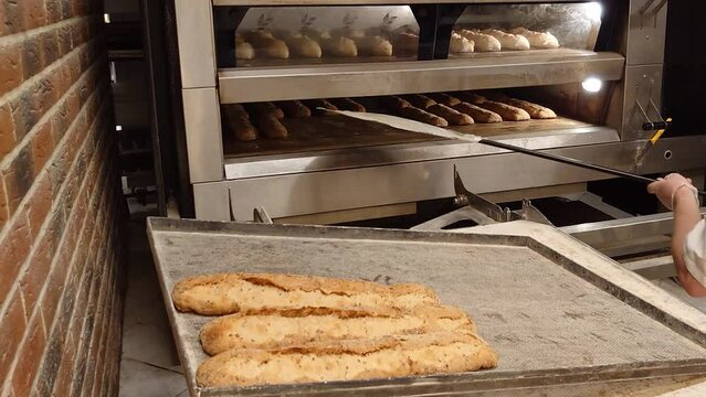 Craft mini-bakery producing French pastries. The baker takes freshly baked hot bread out of the oven. Production of bakery products. Traditional French baguette.