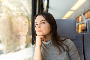 Pensive relaxed female traveler sitting near window on comfortable chair in express train, looking...