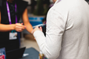 Process of checking in on a conference congress forum event, registration desk table, visitors and attendees receiving a name badge and entrance wristband bracelet and register electronic ticket