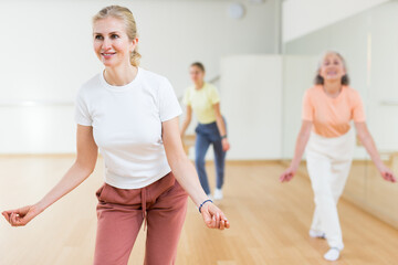 Obraz na płótnie Canvas Portrait of cheerful active blonde female exercising dance moves in fitness studio